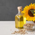 Sunflowers, bottle of oil and seeds on white table, space for text